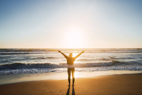 woman on seashore at beach with open arms against in sunset