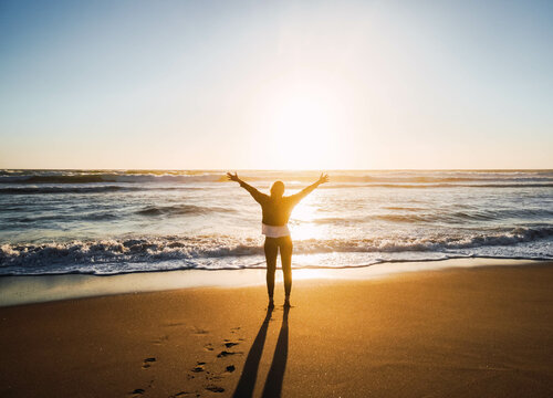 woman on seashore at beach with open arms against sunset