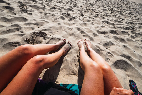two pair of women's legs in the sand on the beach