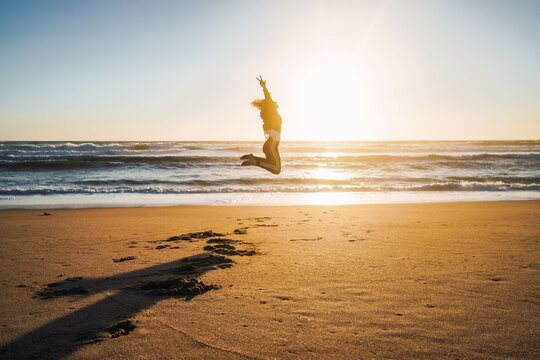woman jumping on the shore of the beach at sunset