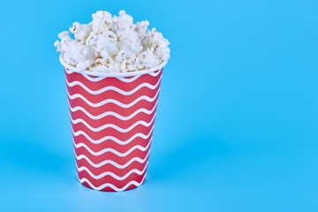 A red glass of popcorn stands on a blue background