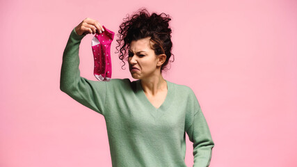 woman feeling disgusted while holding smelly socks isolated on pink - obrazy, fototapety, plakaty