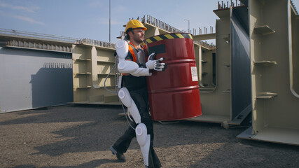 Male contractor in exoskeleton carrying barrel near supervisor