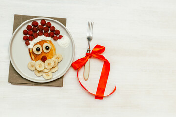 Christmas Santa Claus shaped pancake with sweet fresh raspberry berry and banana on plate on white wooden background for kids children breakfast. xmas food with new year decorations with copy space
