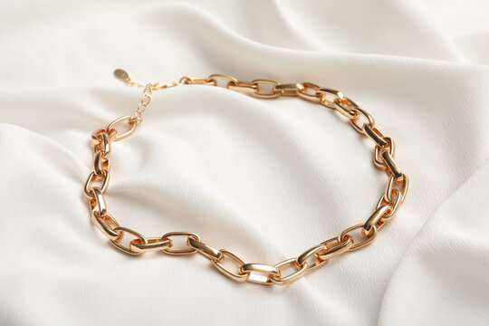 Elegant golden necklace on white fabric. Stylish bijouterie