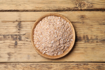 Bowl of wheat bran on wooden table, top view
