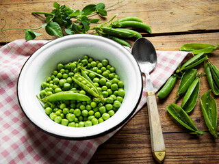 Fresh green peas in a white bowl, pods, on the table