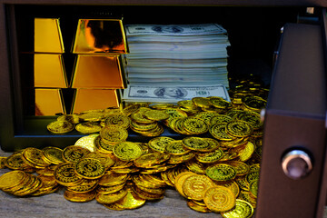 Steel safes box full of coins stack and gold bar and banknote 100 USD on the wooden table