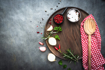 Fototapeta na wymiar Gewürz Zutaten auf einem leeren Holz Schneidebrett und ein Kochlöffel auf einem karierten Geschirrtuch. Draufsicht, Vorbereitung.