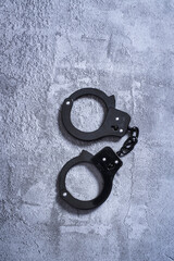 Top view of closed black handcuffs on a grey concrete floor with copy space and room for text
