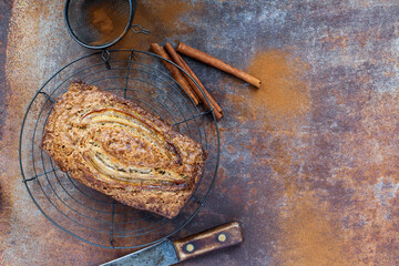 Top view of fresh homemade banana bread cooling on a baker's rack with ingredients nearby. Flat lay with copy space. Selective focus on loaf with blurred background