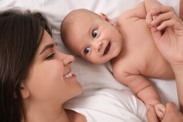 Happy young mother with her cute baby on bed, top view