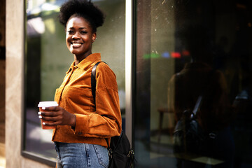 Young african woman outdoors. Beautiful woman with curly hair drinking coffee while walking around town.