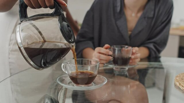 Mid-section slowmo of unrecognizable African-American woman pouring coffee into glass cup in morning
