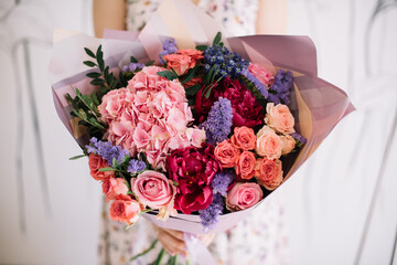 Very nice young woman holding big and beautiful bouquet of fresh hyacinths, hydrangea, roses, carnations, peony flowers in pink, purple and magenta colors, cropped photo, bouquet close up