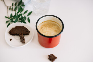 Delicious fresh cup of cappuccino coffee, chocolate cookie and pistachio branches on the white table background, top view, flat lay
