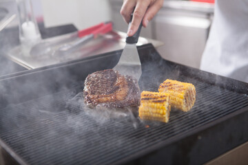 Cropped shot of unrecognizable chef preparing grilled ribeye steak and sweet corn at the kitchen