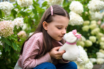 Girl 6 years old with a toy dog ​​portrait near a blooming hydrangea. Concept for end of summer, start of school, new school year
