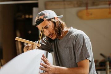 Focused male surfboard shaper suing scribe tool