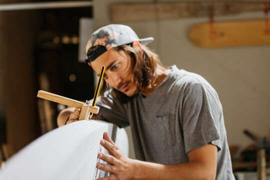 Focused male surfboard shaper suing scribe tool