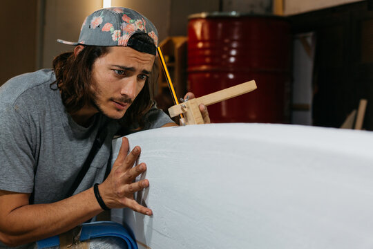 Focused male surfboard shaper suing scribe tool