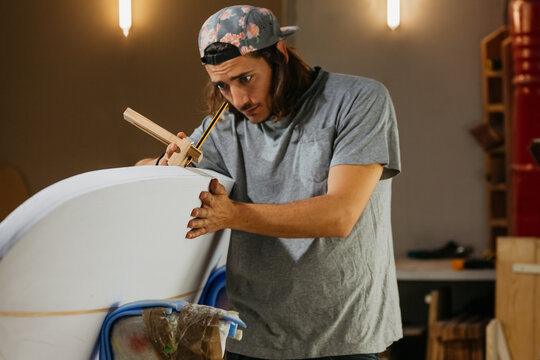 Focused male surfboard shaper suing scribe tool