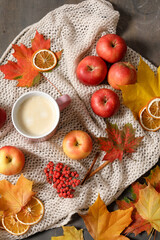 Fototapeta na wymiar Autumn mood flat lay with cup of coffee, fallen leaves, red berries, apples, warm knitted blanket and cinnamon. Autumn holidays, thanksgiving day, home weekend. Flat lay, top view, copy space.
