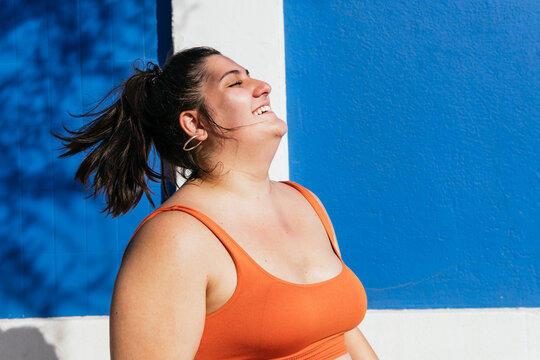Smiling overweight ethnic athlete with closed eyes on street