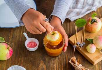 Step-by-step recipe, a boy in a gray long sleeve dips whole apples on skewers in caramel. Children's desserts, party.