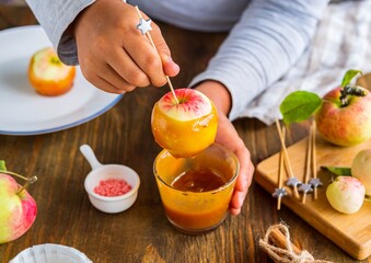 Step-by-step recipe, a boy in a gray long sleeve dips whole apples on skewers in caramel. Children's desserts, party.