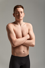 Fototapeta na wymiar Young attractive swimmer in excellent physical shape in purple swimming shorts, on a gray background, copy space