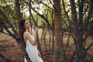 Woman in white dress leaning on a tree forest walk leisure