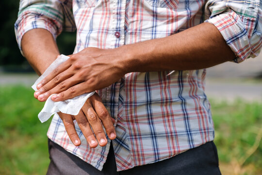 Young African American man disinfecting his hands using a wet wipe close up to prevent infection outdoors in park in summer