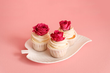 Obraz na płótnie Canvas Delicious creamy cupcakes with rose buds on the leaf shaped plate on pink background.