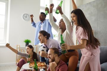 Group of young multiracial male and female football fans watching match on TV, drinking beer and...