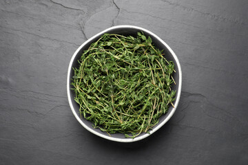 Aromatic thyme in bowl on black table, top view