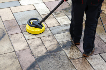 Cleaning stone slabs on patio with the high-pressure cleaner. Person worker cleaning the outdoors...
