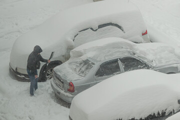 A man brushes his car from the snow. A snowy winter in the city.