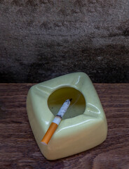 Cigarette that were burning placed on greyish green ashtray on old wooden rustic table. Copy space,...
