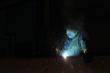 An electric welder welds metal structures at a factory.