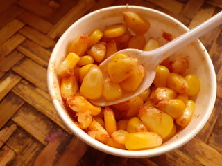 Sweet and spicy corn in a small cup isolated on a wooden surface