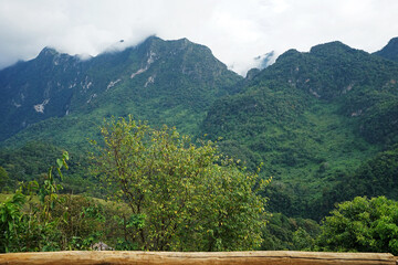 View of high green mountain and cloudy blue sky from wooden balcony