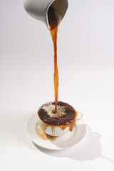Pouring coffee into a white porcelain cup with coffee drink cappuccino on a white saucer plate on a white surface