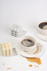 Two cups with coffee drink on a white saucer plate on a white surface surrounded by bubble candles