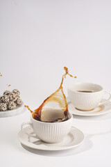 Big coffee splash in a white porcelain cup with coffee drink cappuccino on a white saucer plate on a white surface