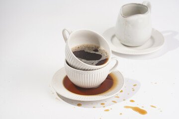 a white porcelain cup with cappuccino stacked in another mug on a white saucer plate on a white surface