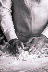 A male chef cook in a white shirt and grey apron making dough out of flour, black and white