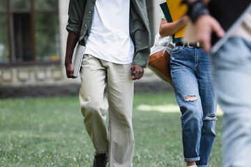 Cropped view of african american student holding laptop near friends outdoors