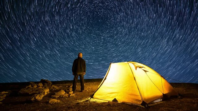 Traveler near the glowing camping tent on the background of the star circles in the night sky. Cinemagraph and Time-lapse.