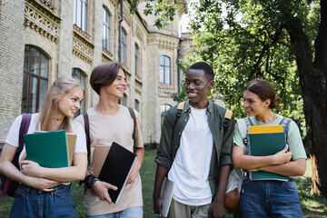 Smiling multiethnic students with laptop and notebooks outdoors